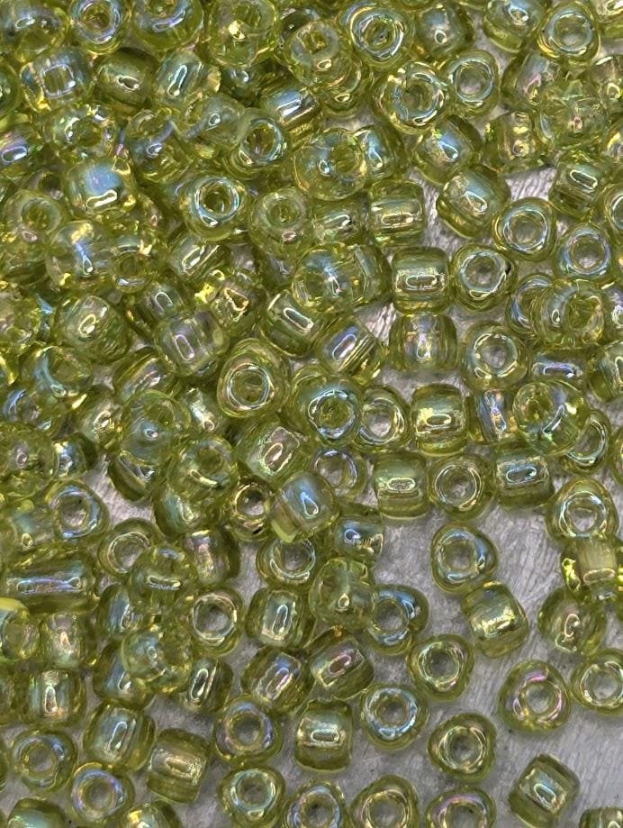 The image is a close-up of numerous small, clear beads in various shades of green. The beads are scattered across a surface, creating a visually interesting and vibrant display.