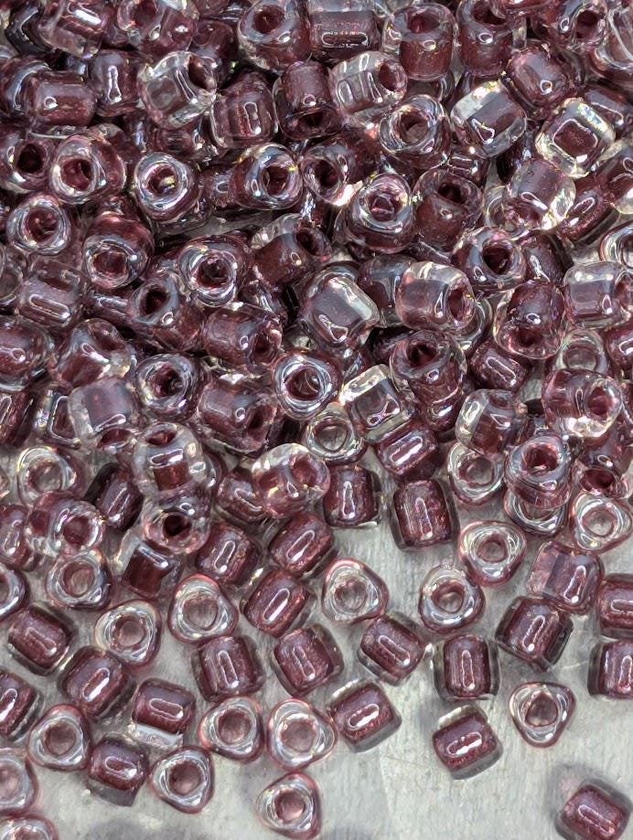 The image is a close-up of numerous small, clear beads in various shades of purple, scattered across a surface.