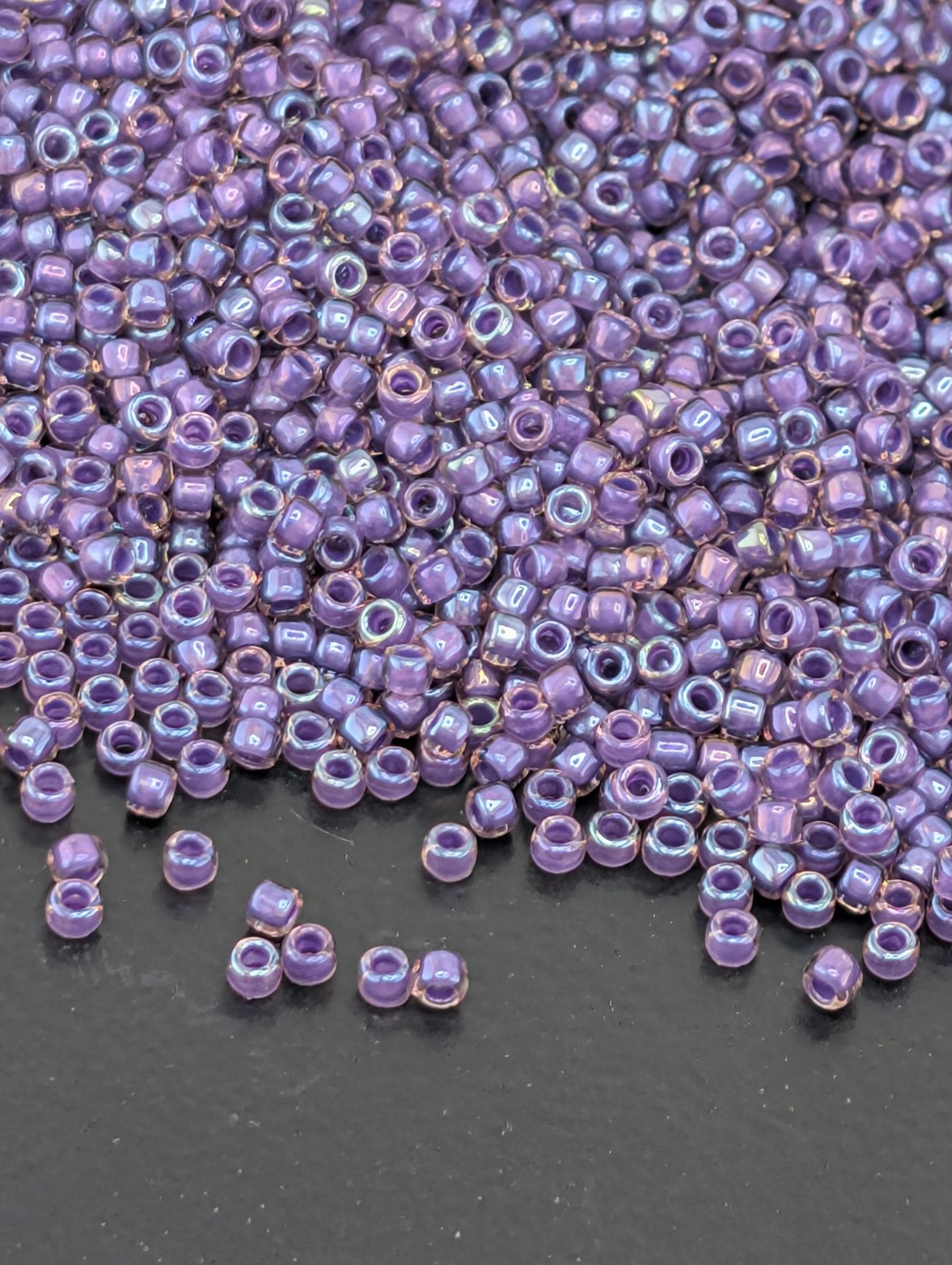 a large pile of small, round beads in various shades of purple, scattered on a dark surface.