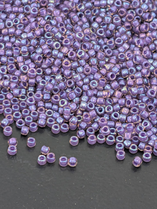 a large pile of small, round beads in various shades of purple, scattered on a dark surface.