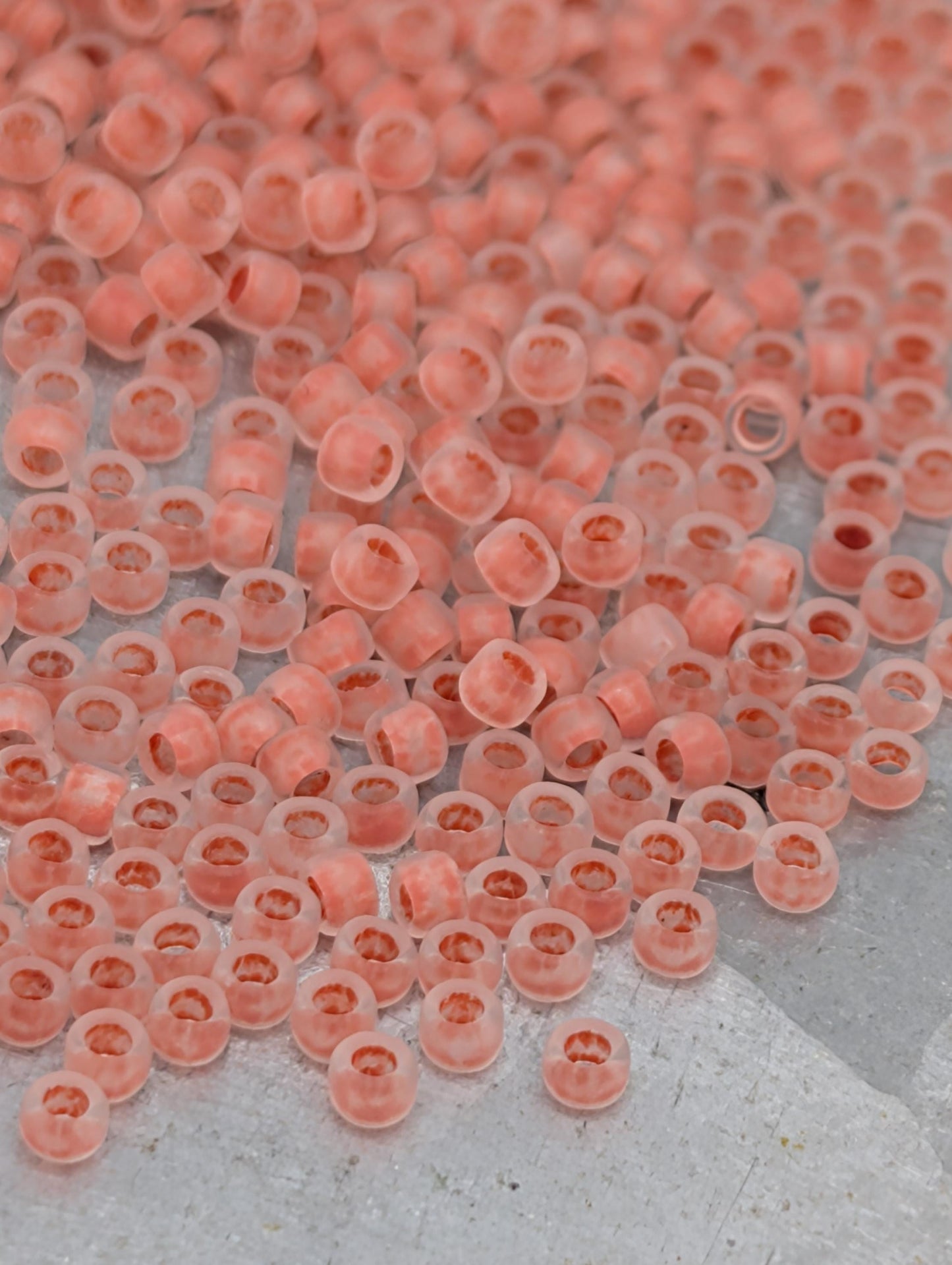 a large number of small, clear beads in shades of pink and orange, scattered across a surface.