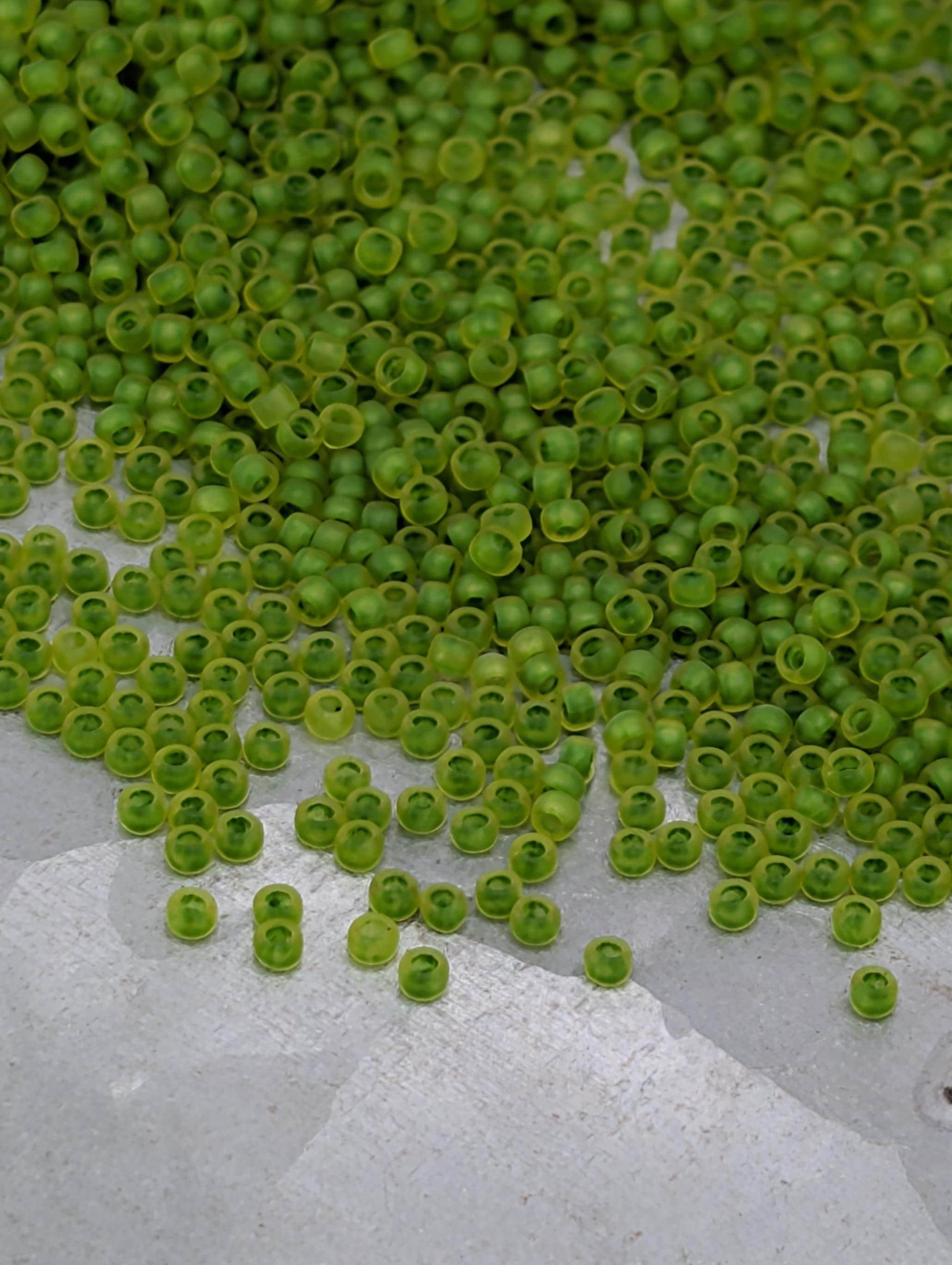 a large pile of green beads or seeds scattered on a white surface.