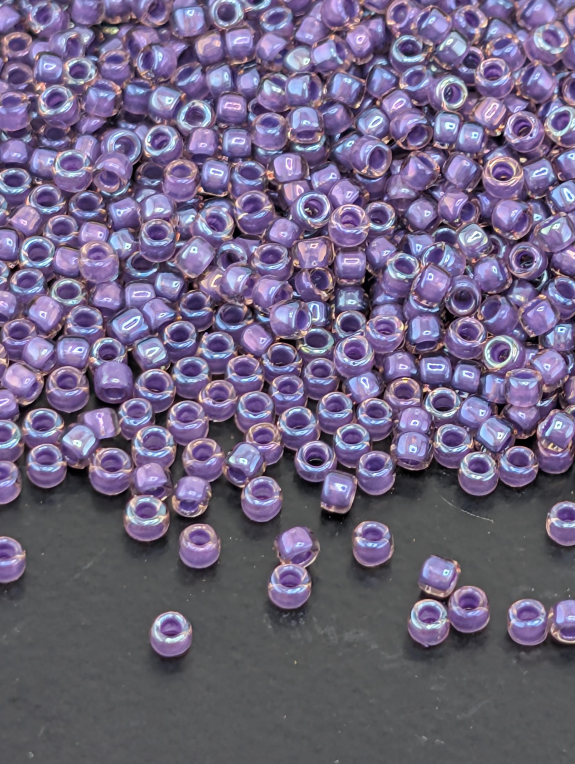 a large pile of small, round, purple beads scattered on a dark surface.