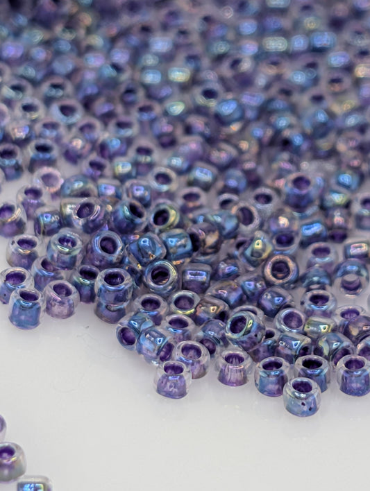 a close-up view of numerous small, round beads in various shades of purple, scattered across a white surface.