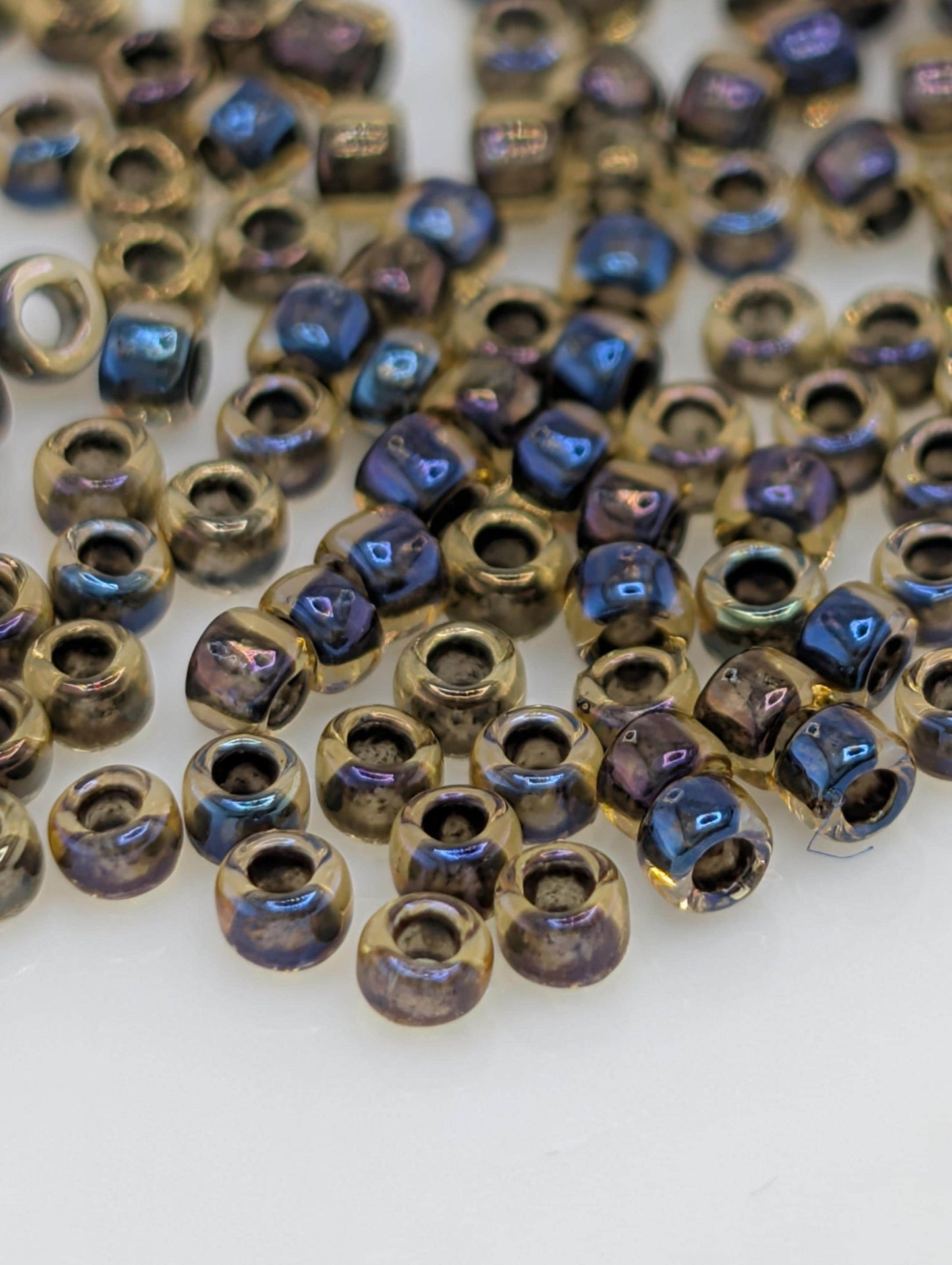 a collection of small, clear beads in various colors, including gold, blue, and purple, scattered across a white surface.