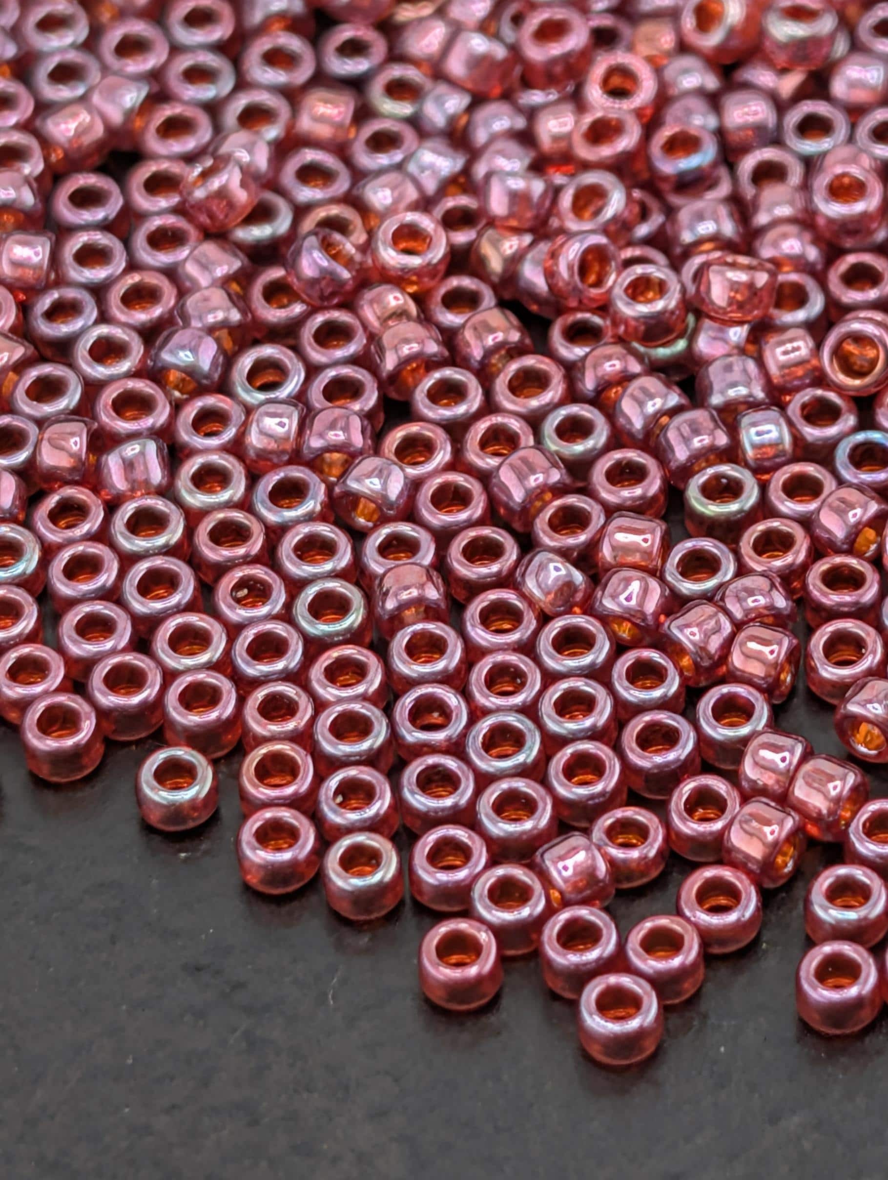 a close-up view of numerous small, round beads in shades of pink and red, scattered across a dark surface.