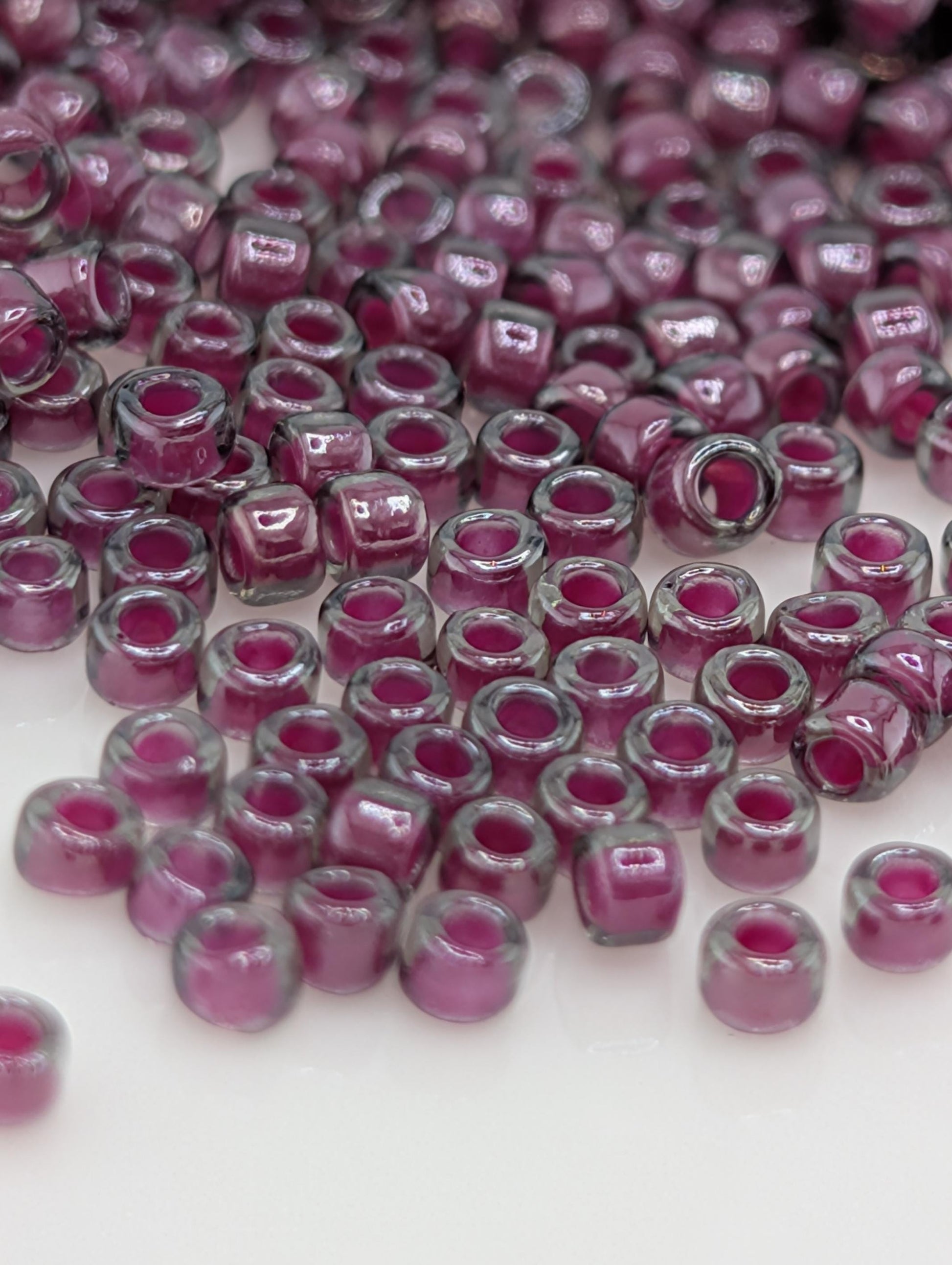 a close-up view of numerous small, clear beads in shades of purple and gray, scattered across a white surface.