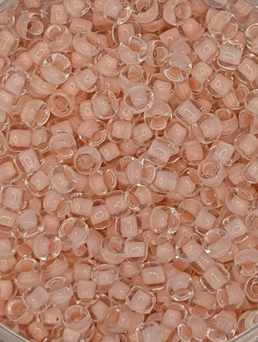 The image is a close-up of a pile of clear, small beads in various shades of pink and white.