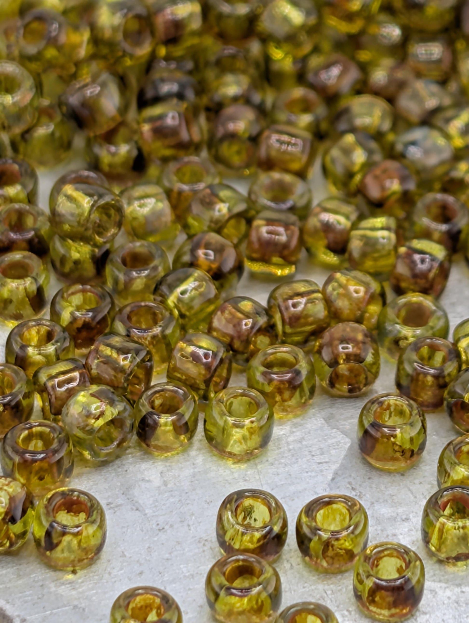 a collection of small, clear glass beads in various shades of green and brown, scattered across a surface.