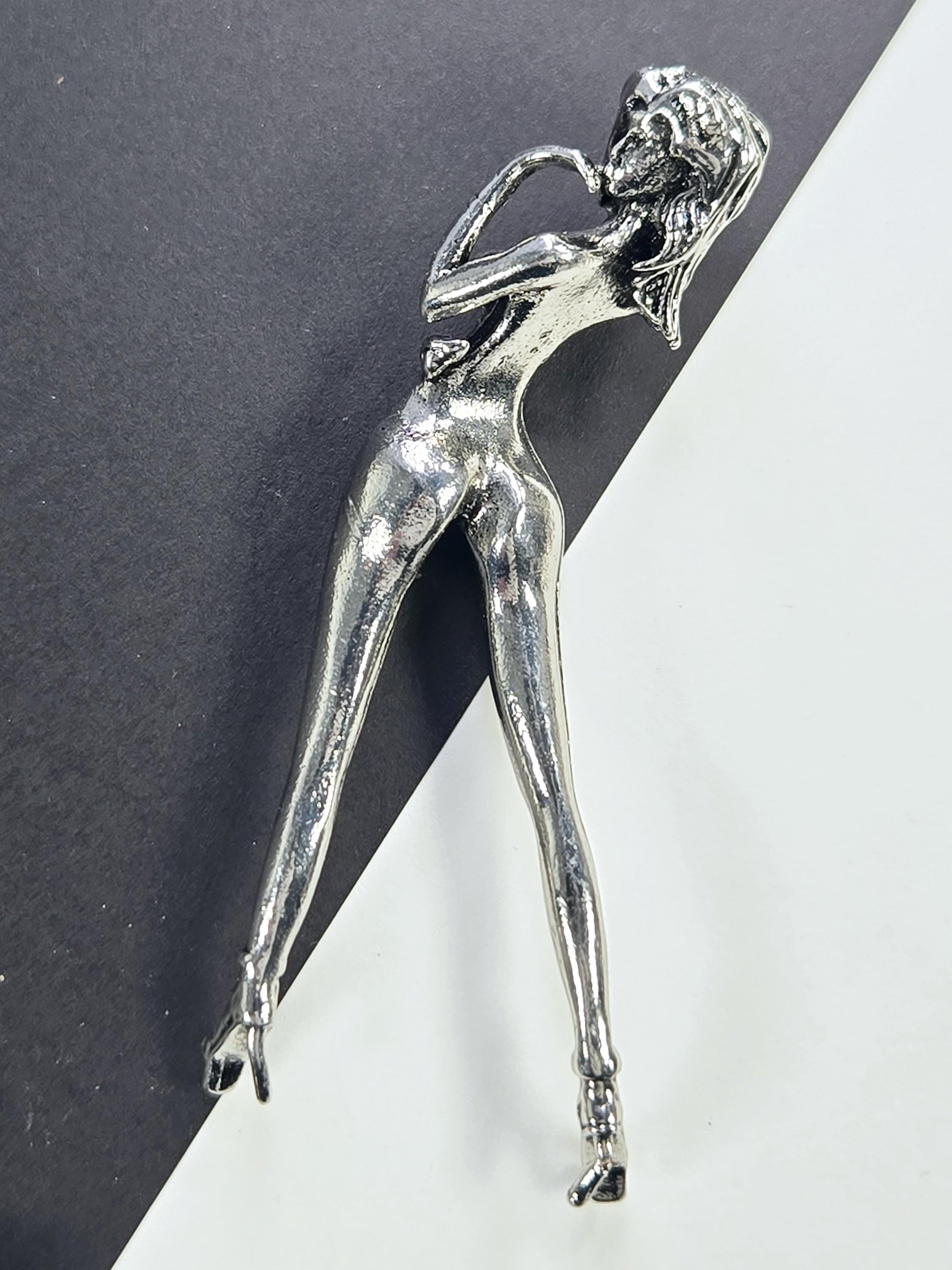A silver metal figurine of a woman lying down on a black surface.