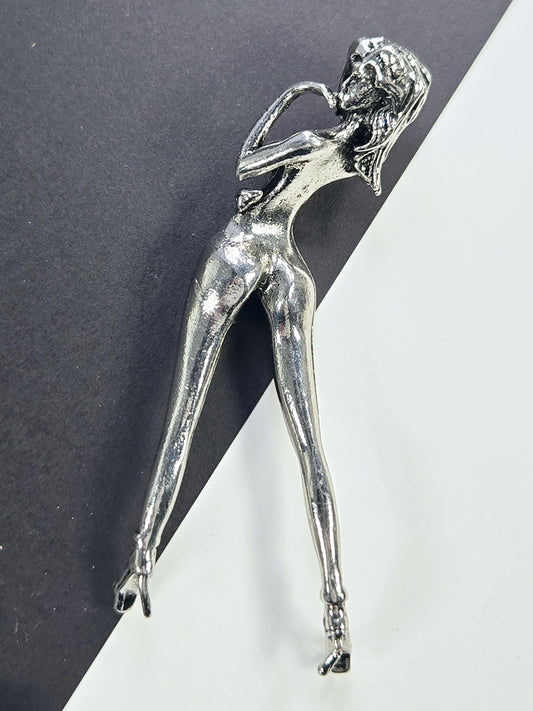 A silver metal figurine of a woman lying down on a black surface.