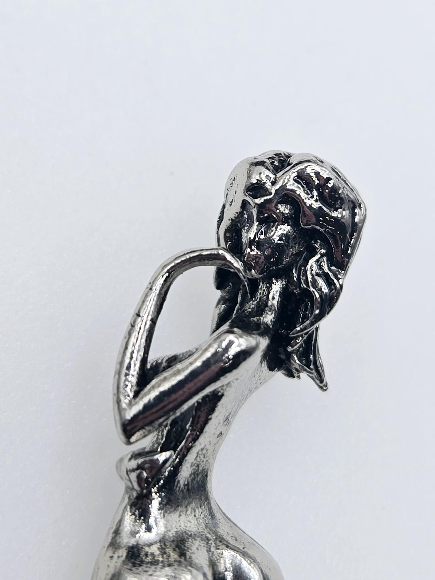 A close-up view of a shiny, metallic sculpture or figurine with a textured, sculpted appearance.