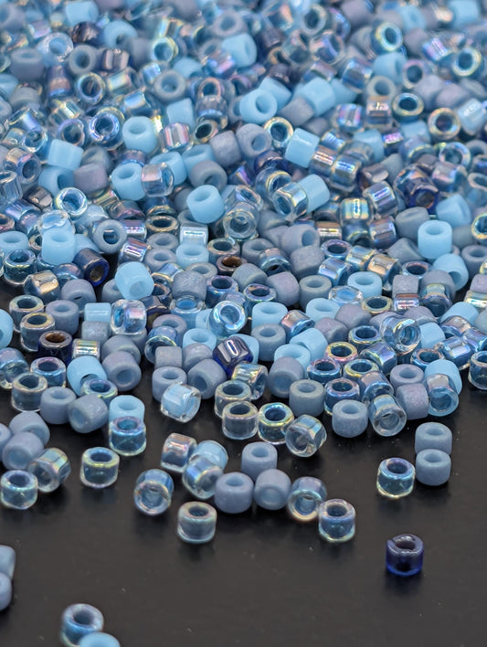 a large pile of small, clear beads in various shades of blue and gray, scattered on a dark surface.