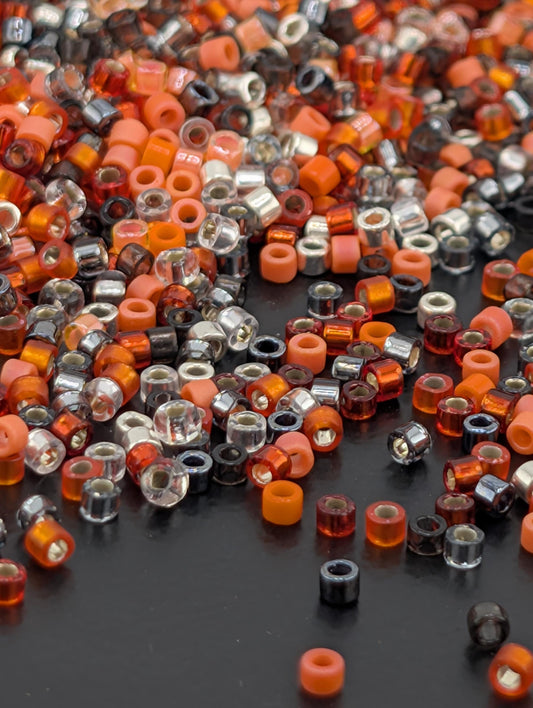 The image is a close-up of a collection of colorful beads, including orange, black, and silver beads, scattered on a dark surface.