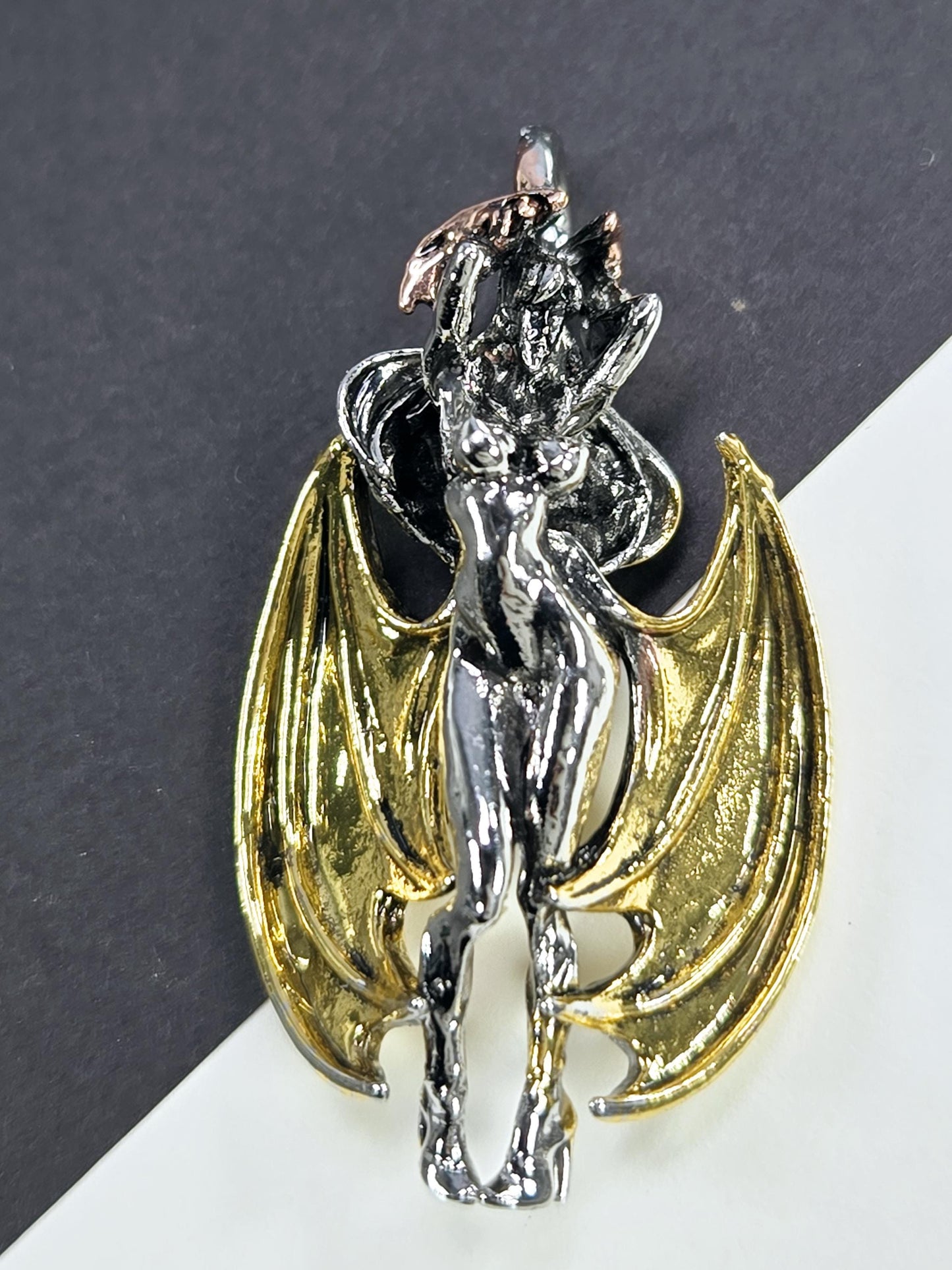 A metallic, winged figure resembling a bat or dragon, with a shiny, golden-colored body and wings.