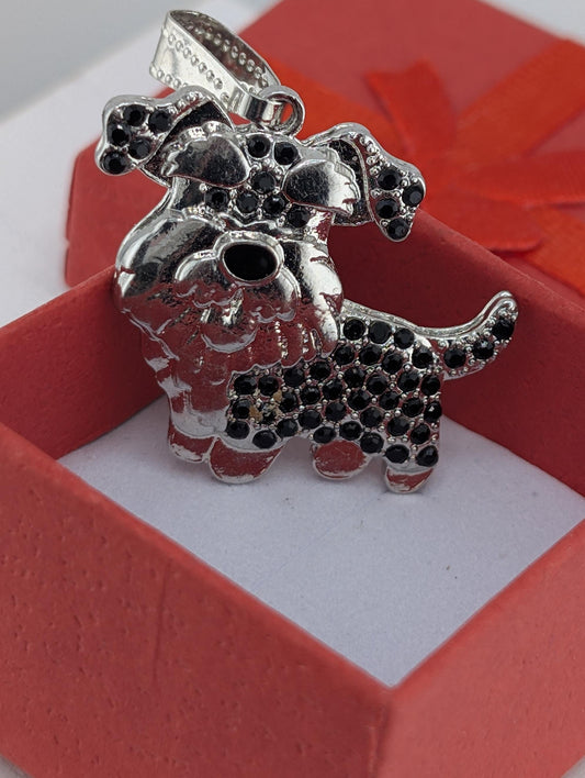 A silver-colored pendant in the shape of a dog, adorned with black gemstones, is displayed in a red box.