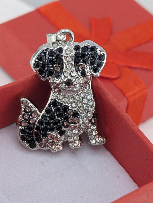 A silver charm in the shape of a dog, adorned with black and silver rhinestones, is displayed in a red gift box.