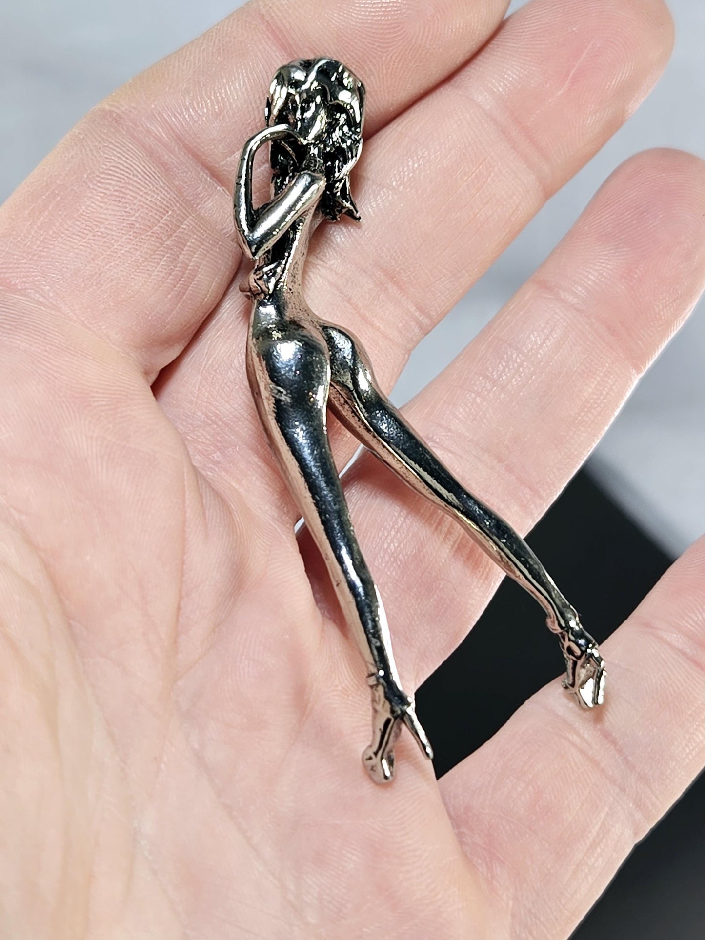 A hand holding a small silver figurine of a woman.