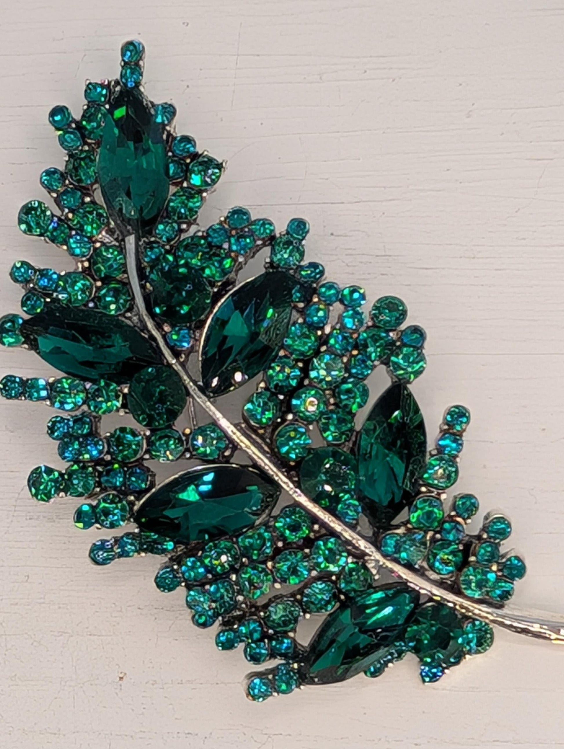 A decorative brooch with a leaf-like design, featuring a variety of green gemstones and metallic elements.