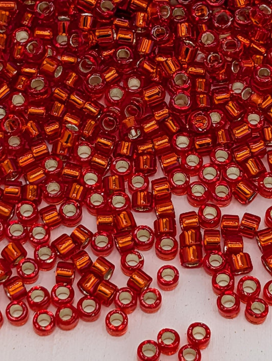 The image is a close-up of numerous red and orange beads scattered across a surface.