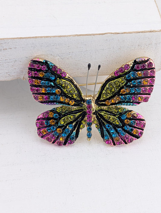 A colorful butterfly brooch with a metallic frame and a vibrant pattern of gemstones.