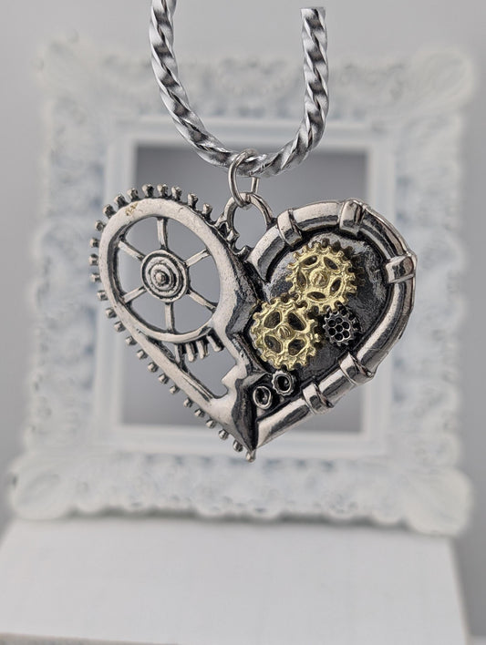 A silver heart-shaped pendant with gears and a wheel attached to it, hanging from a chain.
