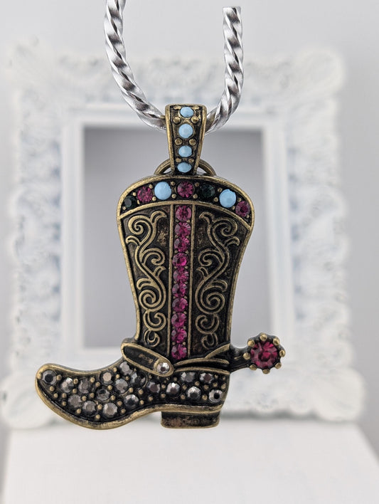 A decorative pendant in the shape of a cowboy boot, adorned with colorful gemstones and a chain.