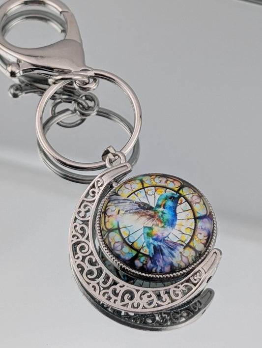 A keychain with a decorative metal frame and a circular pendant featuring a colorful hummingbird design.