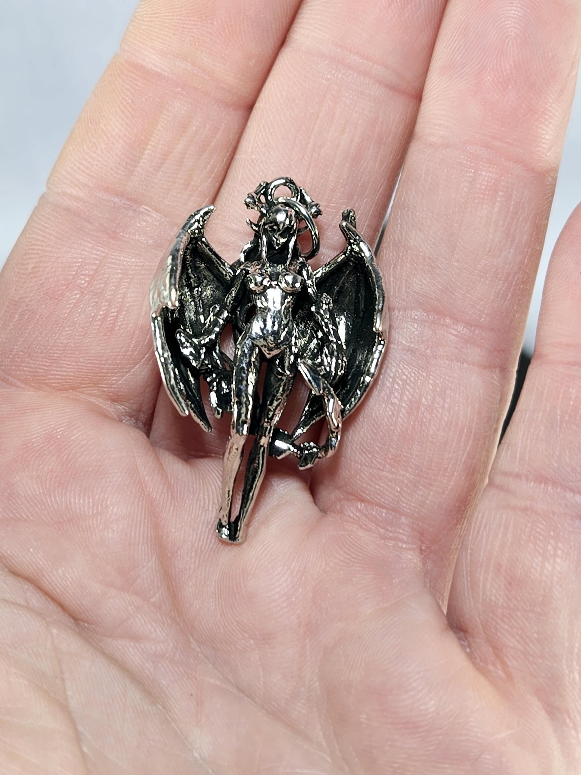 A close-up image of a person&#39;s hand holding a small, metallic, winged object resembling a dragon or mythical creature.