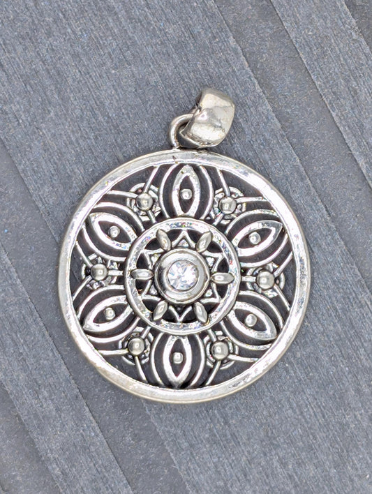 A silver pendant with an intricate design, featuring a central motif surrounded by smaller, symmetrical patterns.