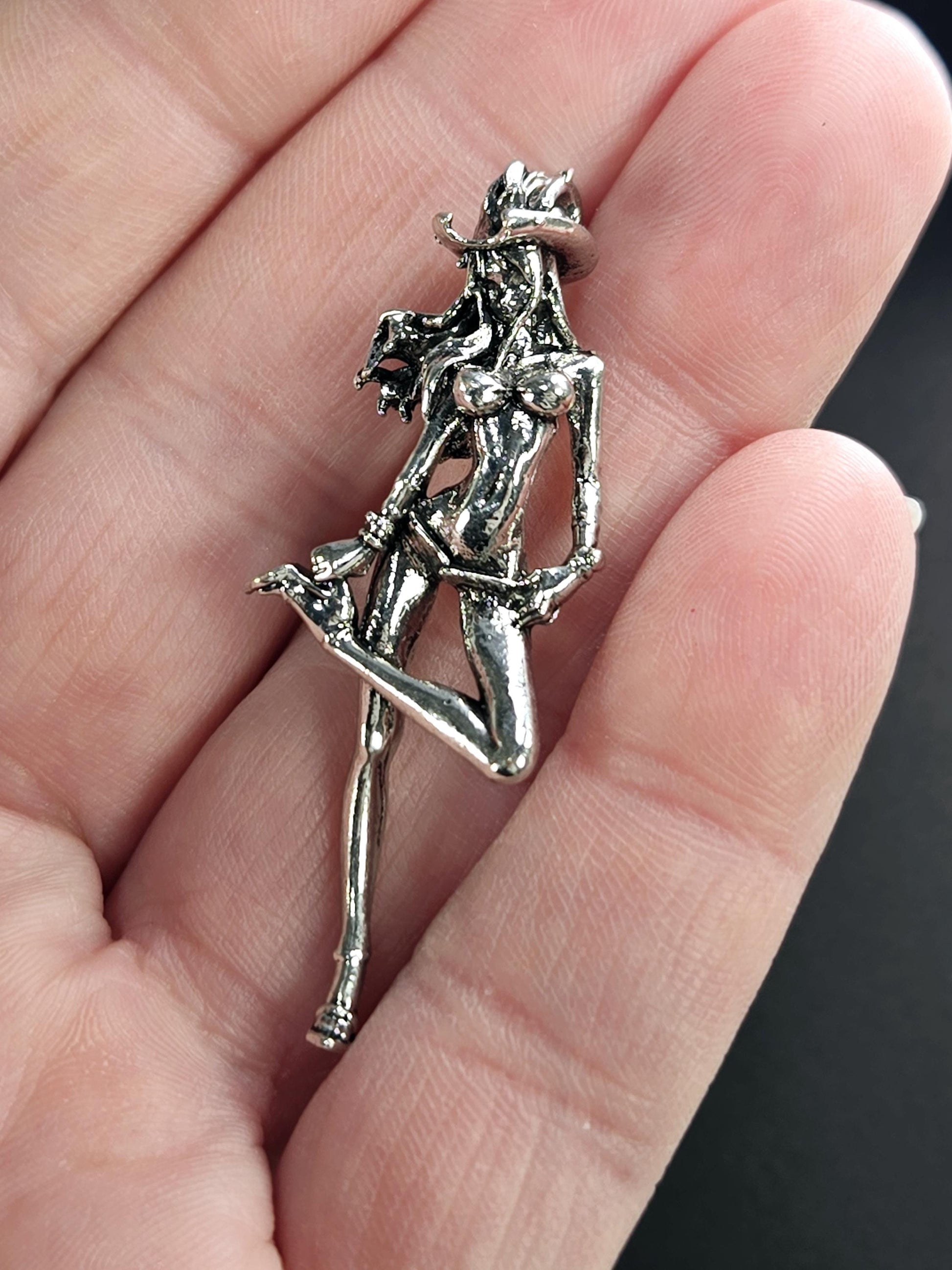 A close-up image of a person&#39;s hand holding a silver-colored metal pin or brooch in the shape of a woman.