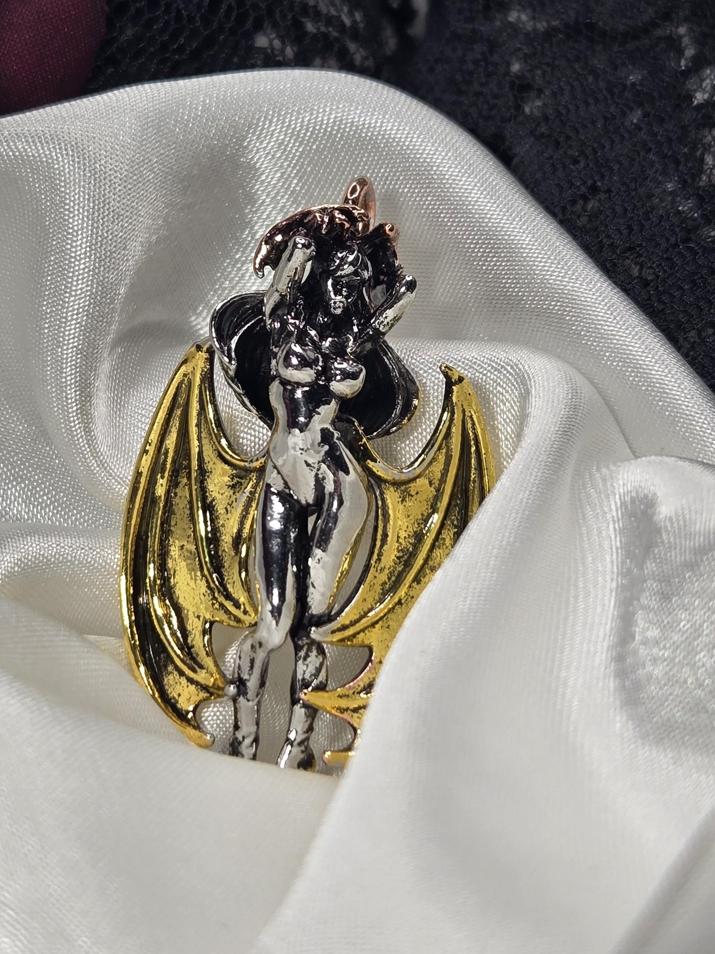 A close-up image of a decorative piece, possibly a brooch or pendant, featuring a winged figure with a metallic, black-and-gold design.