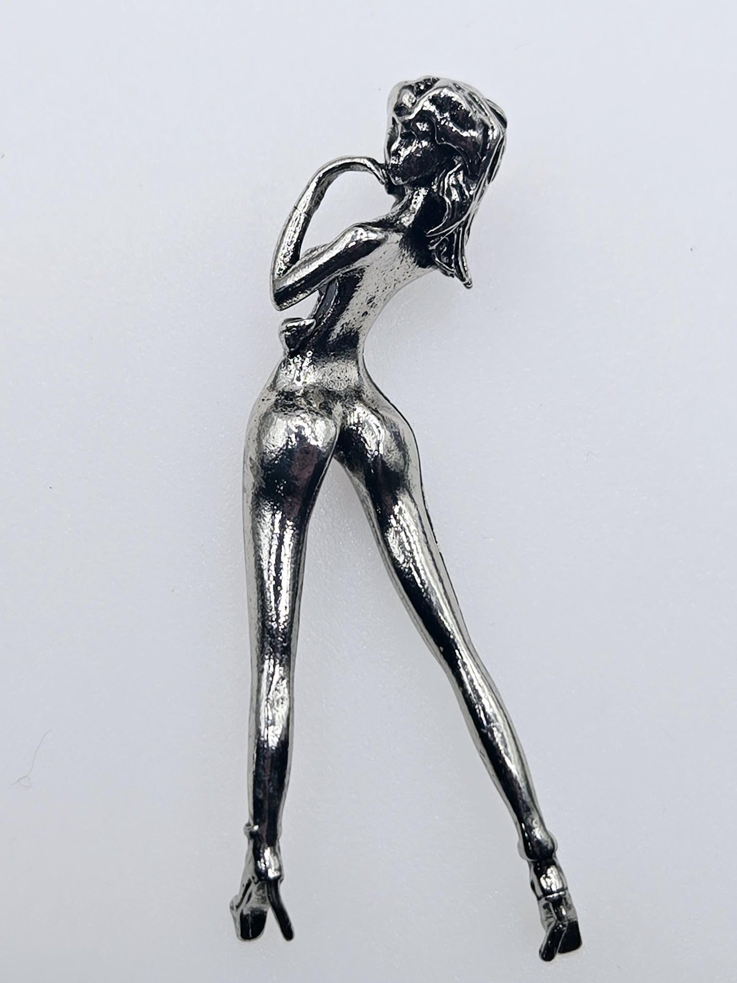 A shiny silver metal brooch in the shape of a woman.