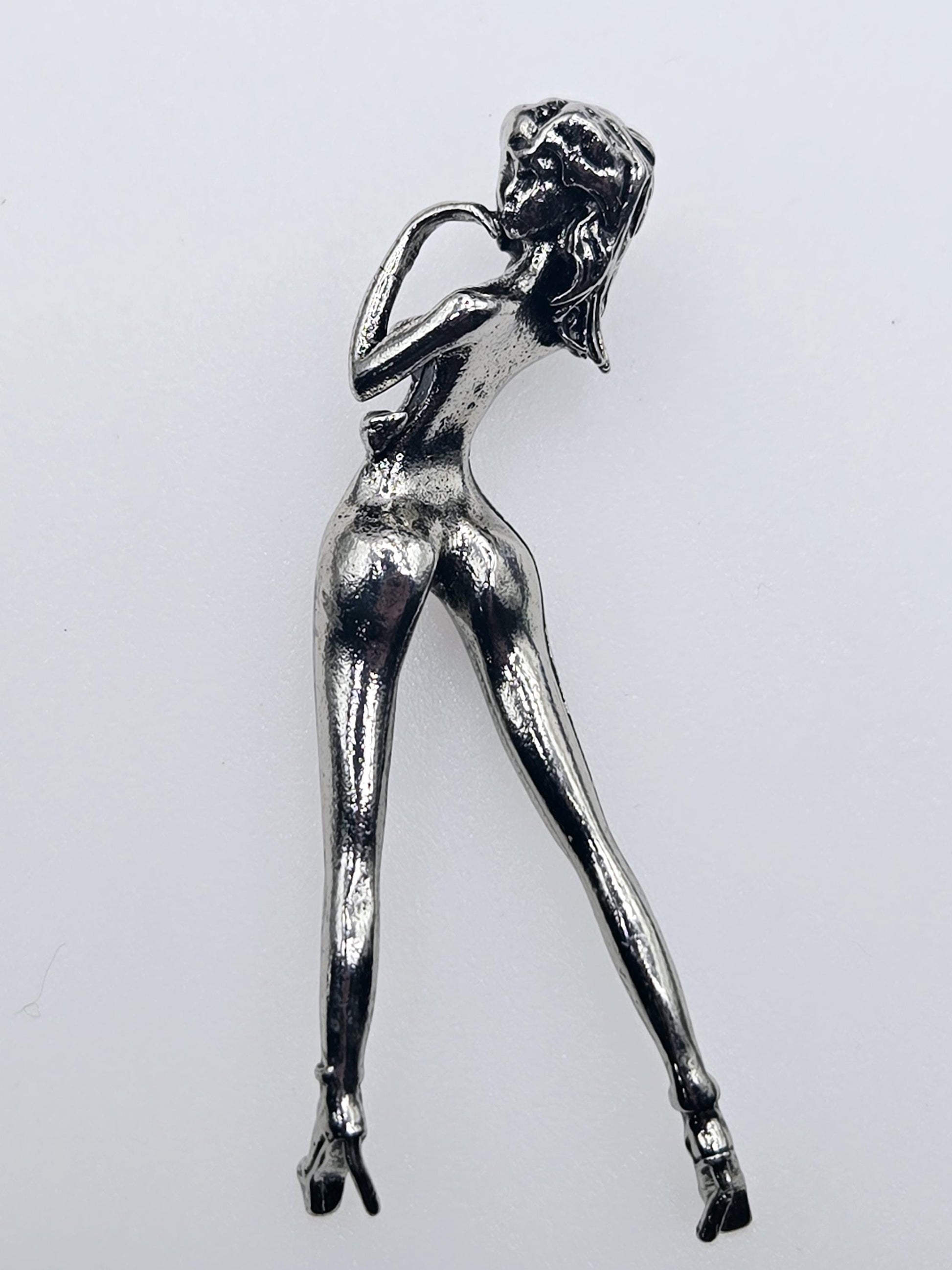 A shiny silver metal brooch in the shape of a woman.