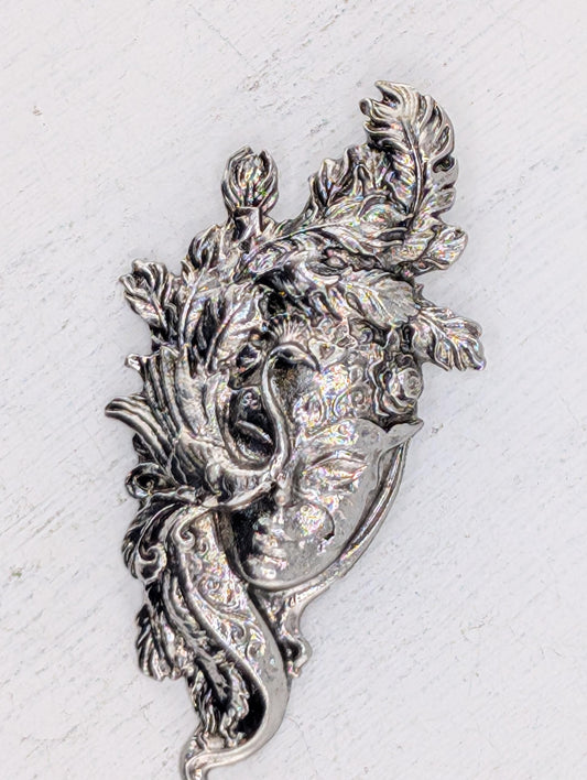 a decorative metal piece with intricate floral and leaf-like designs, including a face-like element.