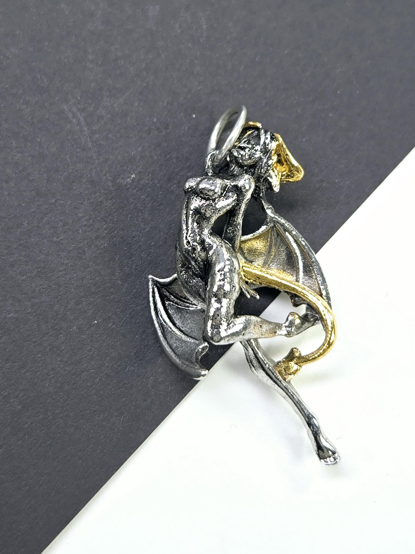 A silver and gold metal sculpture of a winged creature, possibly a mythical or fantastical being, is displayed on a black surface.