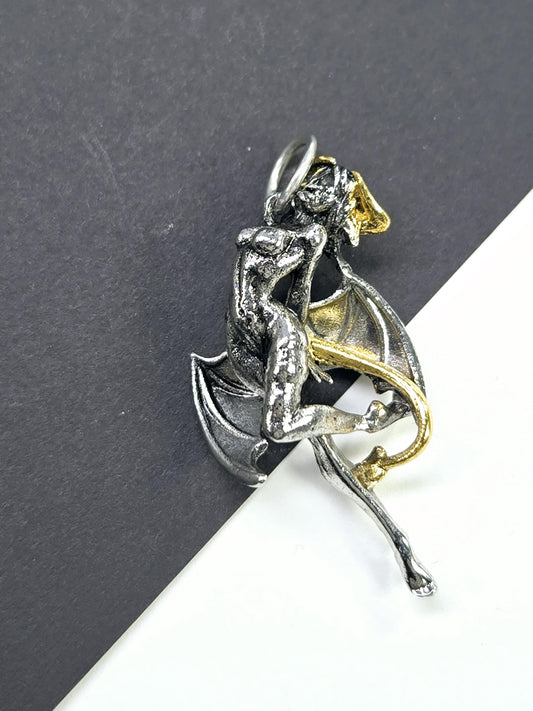 A silver and gold metal sculpture of a winged creature, possibly a mythical or fantastical being, is displayed on a black surface.