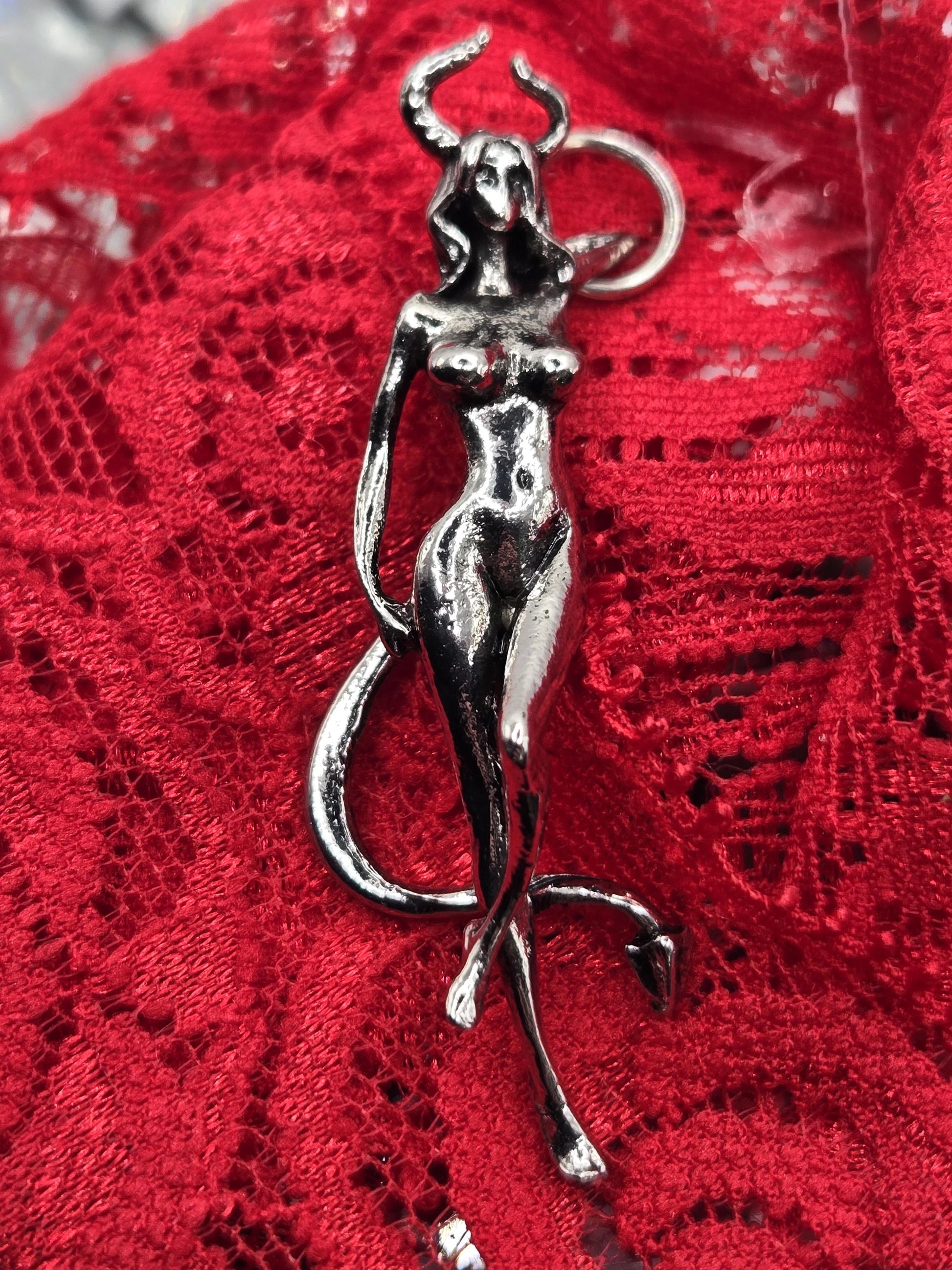 A silver metal sculpture of a human figure is displayed on a red lace background.
