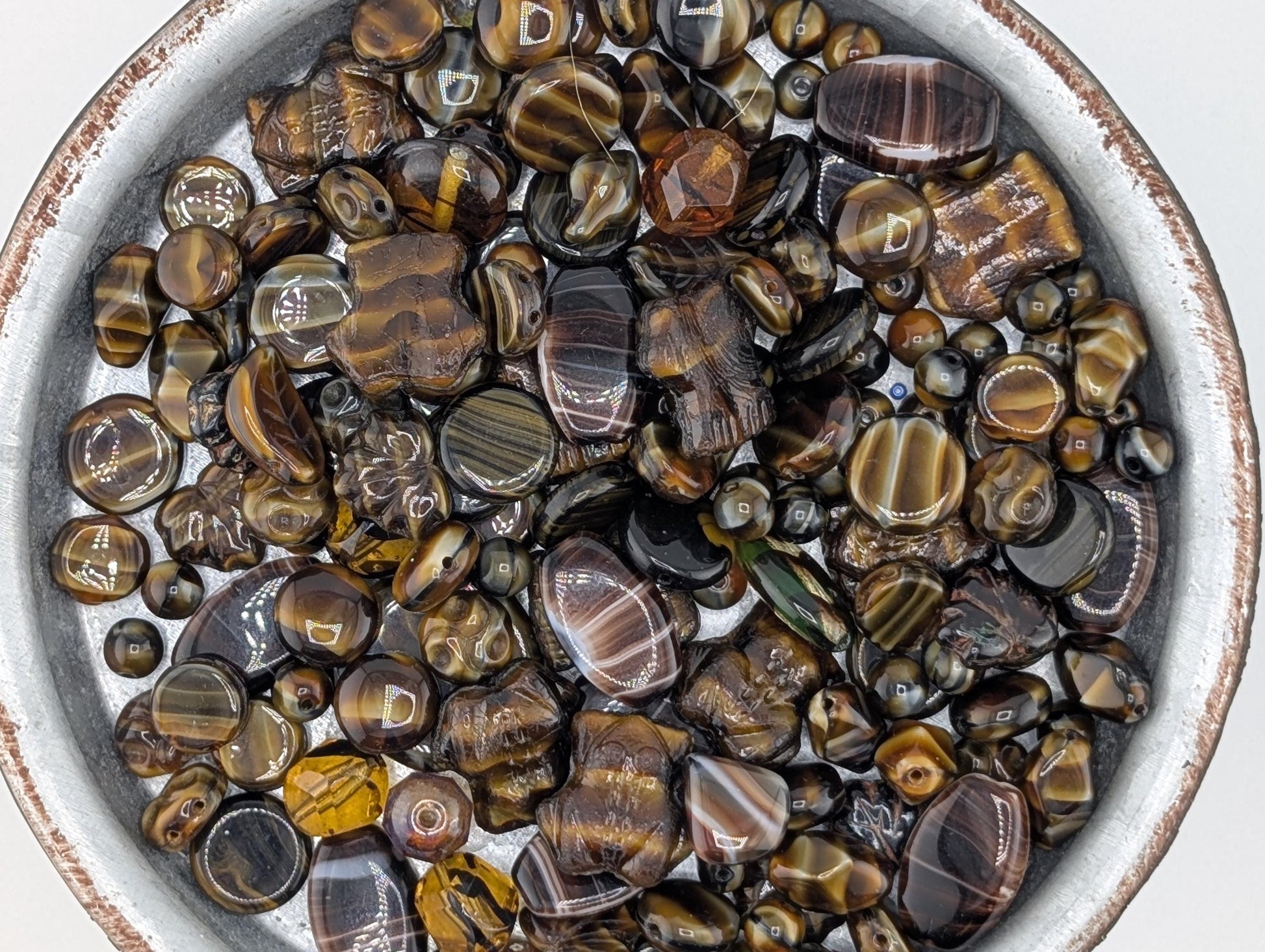 A bowl filled with various colored and shaped beads, including black, brown, and gold-toned stones.