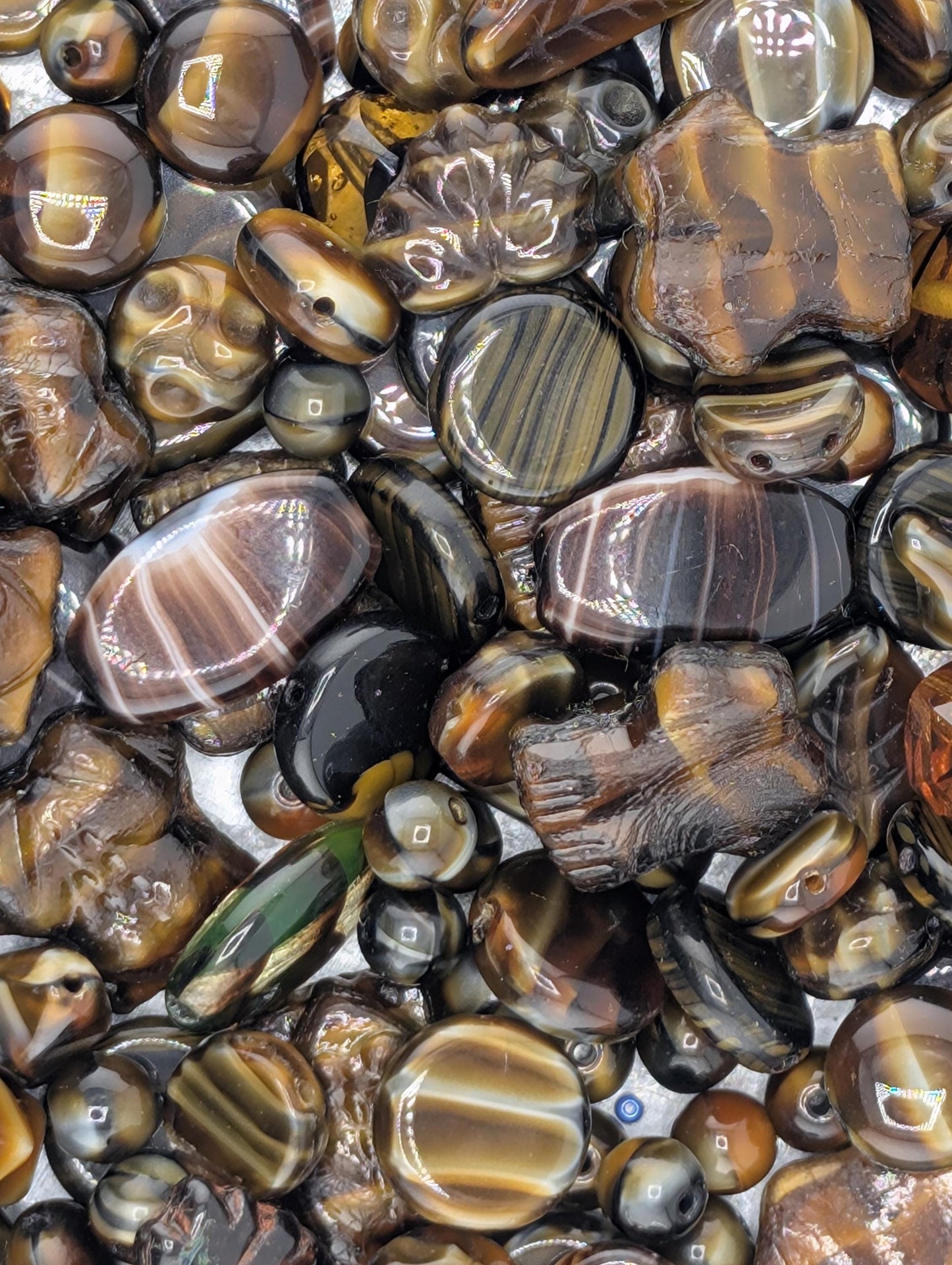 The image is a close-up view of a collection of various colored beads and stones, including amber, black, and brown hues.