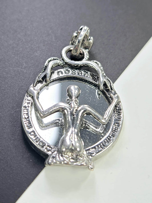 A silver-colored pendant or charm with an intricate design, featuring a figure or symbol within a circular frame.