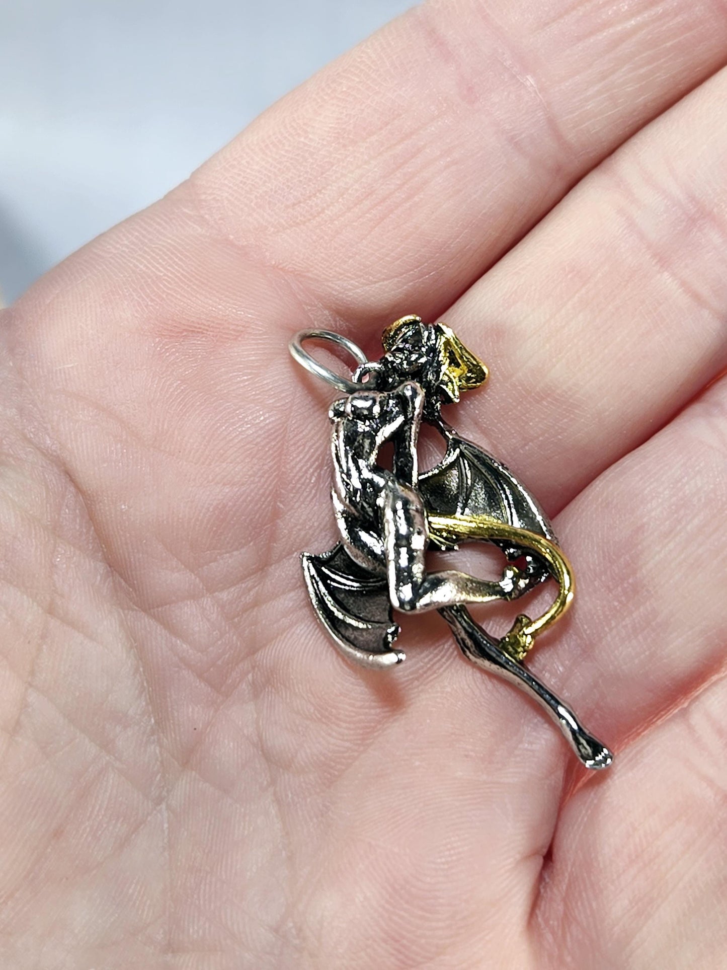 A hand holding a small, intricately designed metal piece featuring a dragon-like creature with wings and a tail.