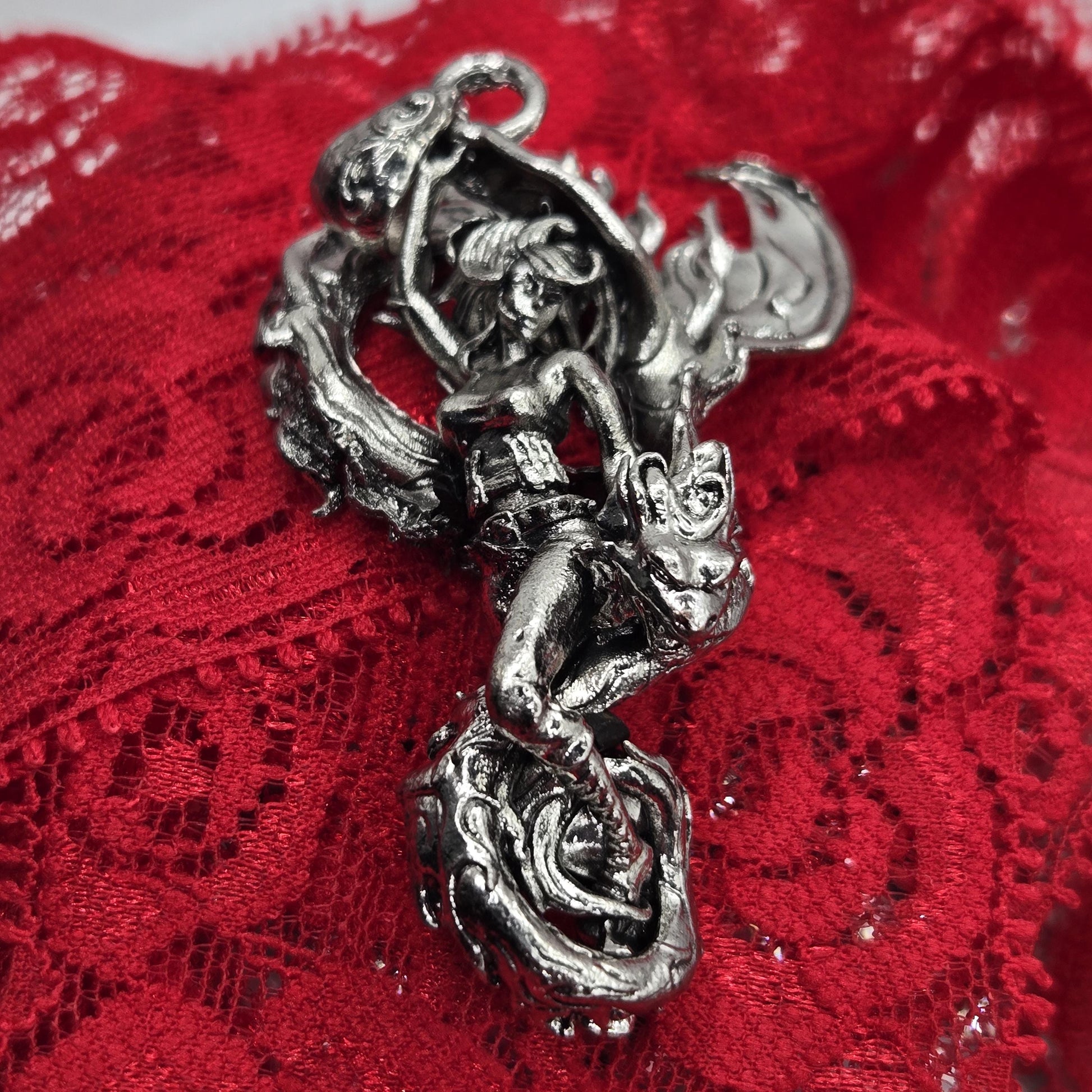 A close-up image of a silver, intricately designed metal piece, resembling a dragon or mythical creature, resting on a red fabric surface.