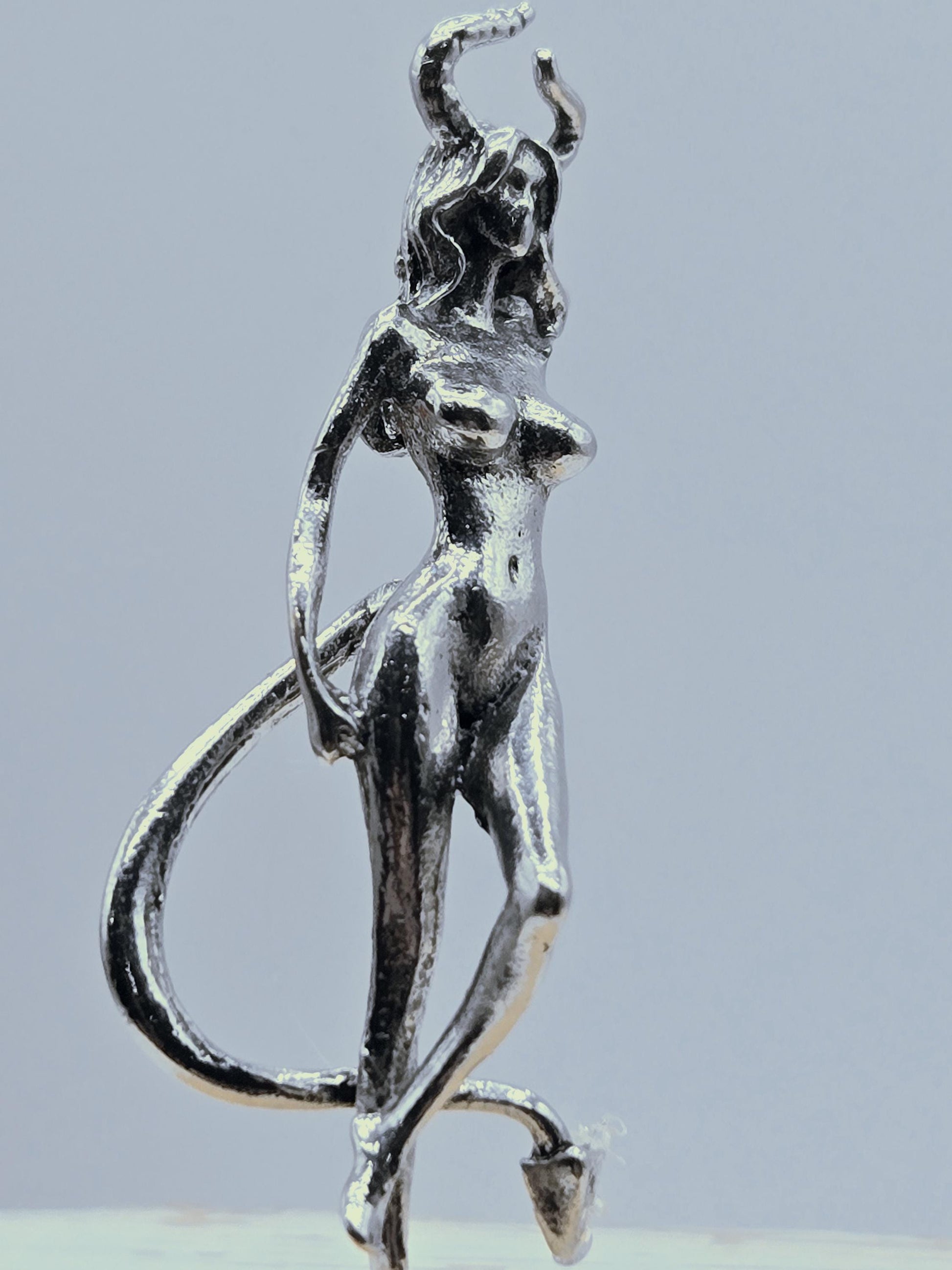 A silver-colored metal sculpture of a human figure, with a twisted and distorted appearance, is shown against a light blue background.
