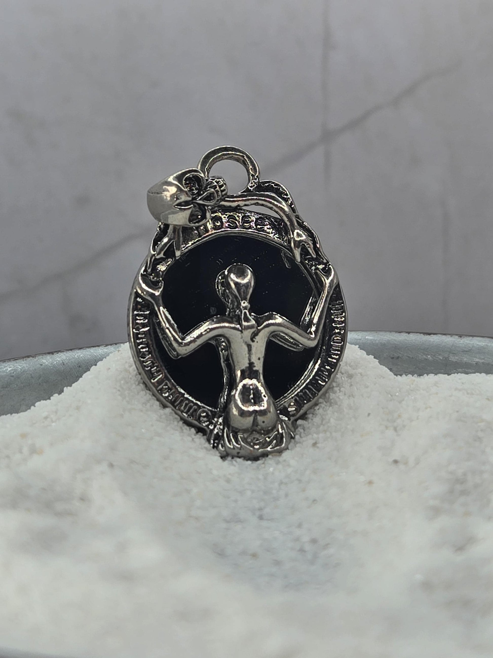 A silver-colored charm or pendant with an intricate design, resting on a white surface.