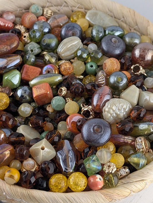 A woven basket filled with a variety of colorful glass beads, including multicolored glass beads, glass beads in shades of green, orange, and yellow, and glass beads in shades of brown, gray, and white.