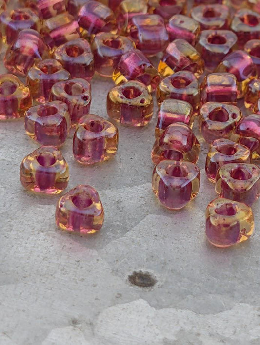 a collection of small, clear beads in various colors, including shades of pink and yellow, scattered on a surface.
