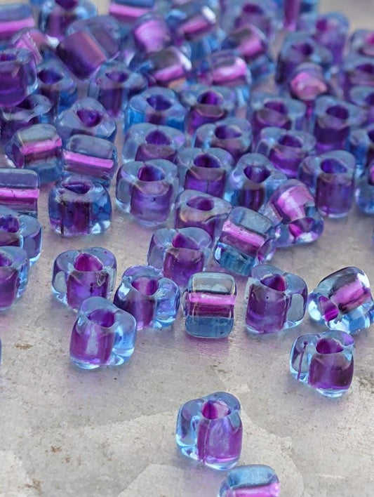a collection of small, clear beads in various shades of purple and blue, scattered across a surface.