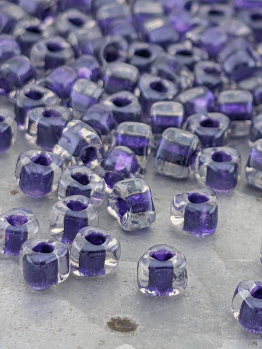 a collection of clear glass beads in various shades of purple, scattered across a surface.