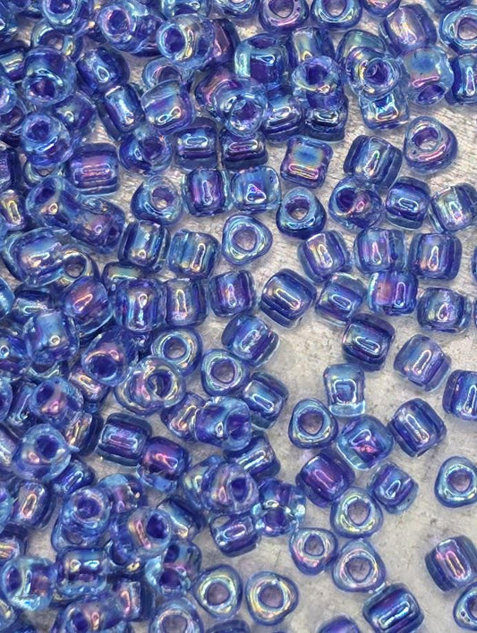 The image is a close-up of numerous small, clear beads in various shades of blue, scattered across a surface.